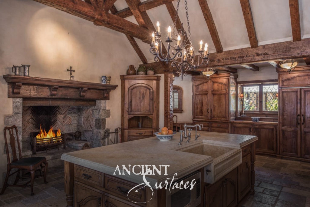 Kitchen island topped in reclaimed limestone with an integrated stone farmhouse sink, facing an antique stone fireplace and reclaimed flagstone flooring
