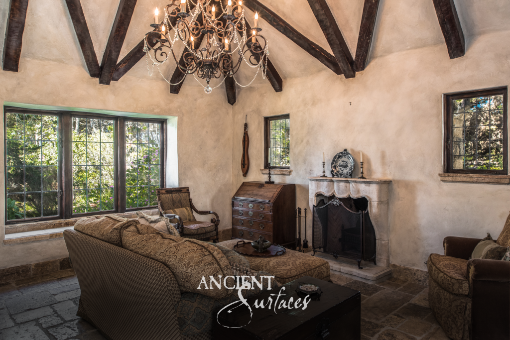 Carved antique limestone fireplace mantel in a beamed sitting room over reclaimed limestone flagstone floors