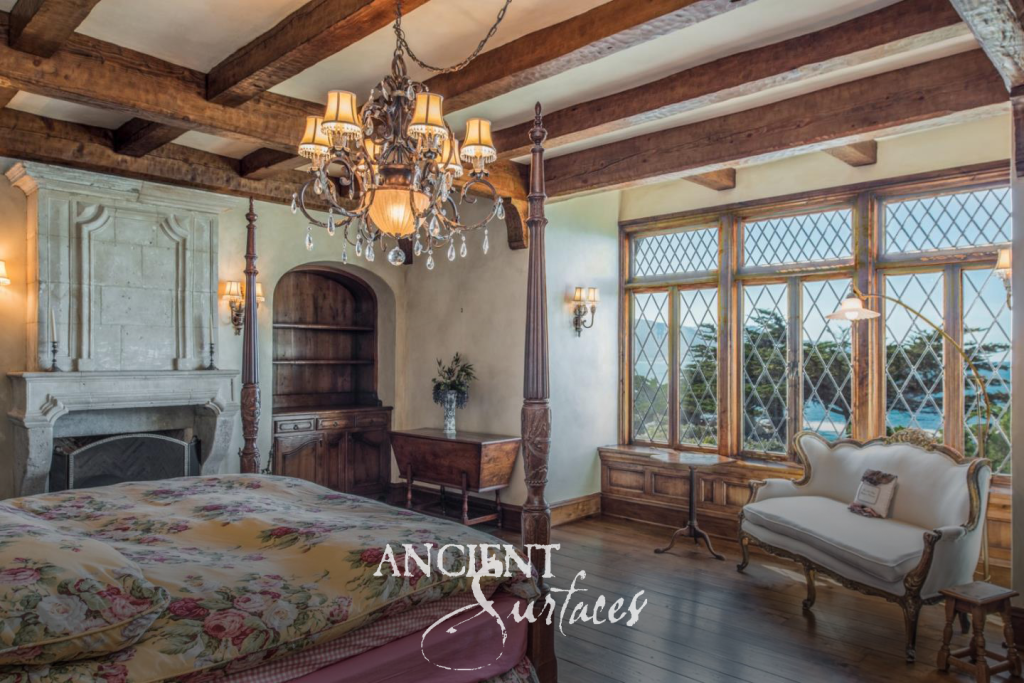 Tall reclaimed limestone fireplace mantel and carved overmantel in a bedroom with leaded glass windows above the ocean