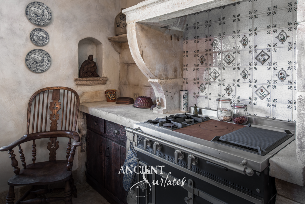 Limestone cooking hood carved by hand with scrolled corbels above a reclaimed limestone countertop and antique delft tile backsplash