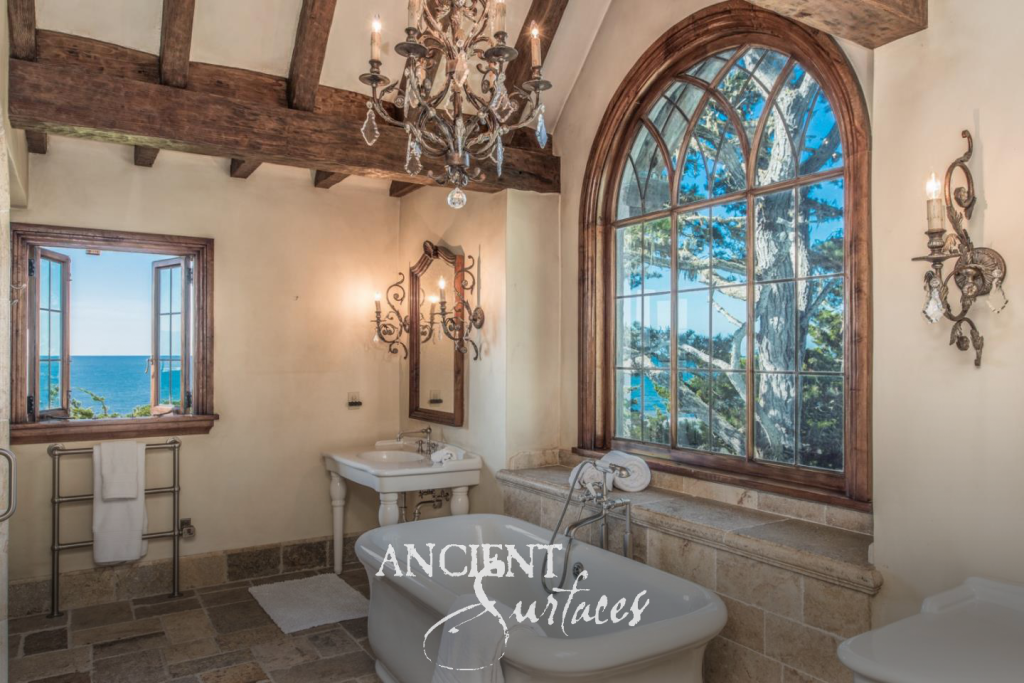 Reclaimed limestone flooring and a limestone tub surround beneath an arched window looking out to the sea