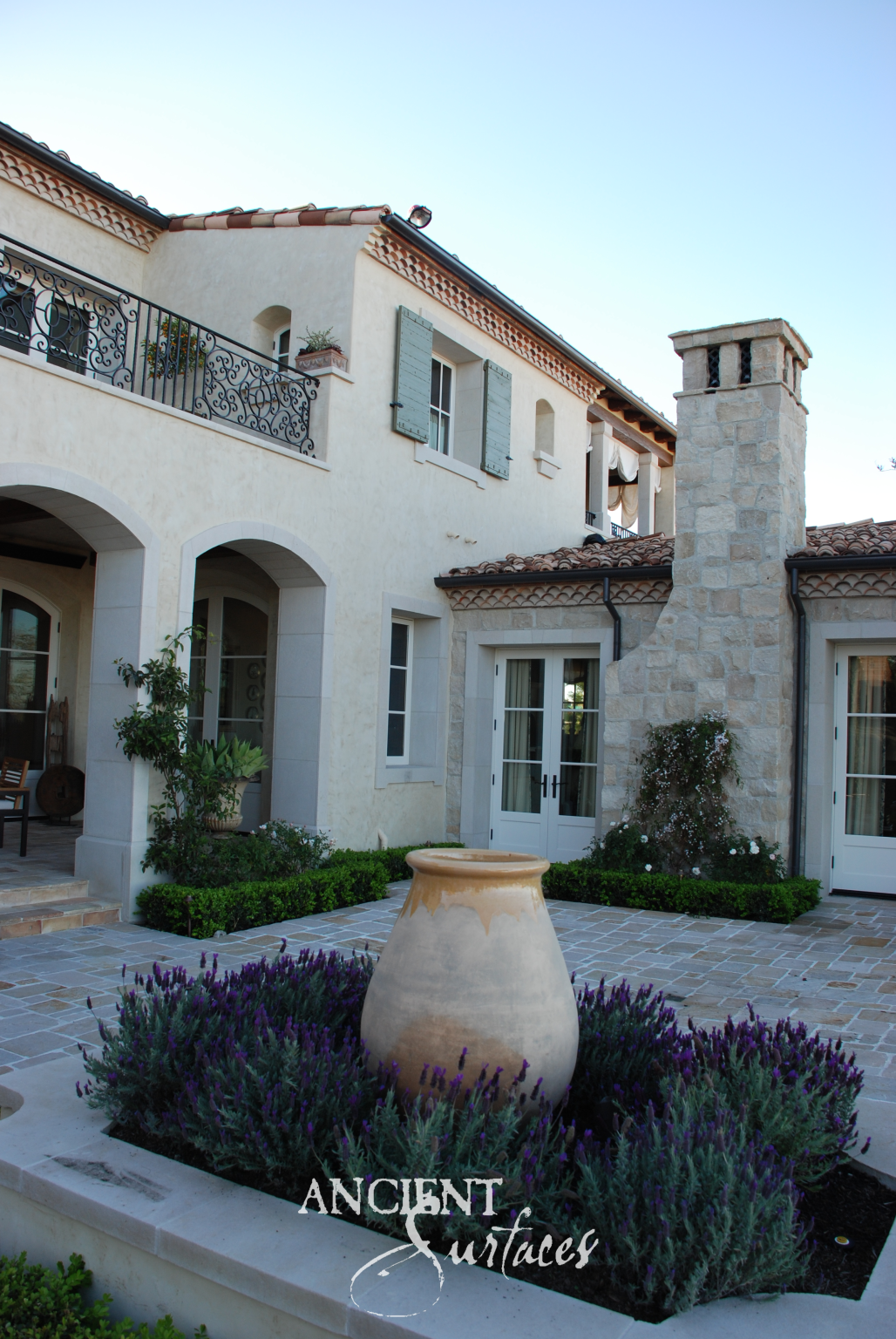 Reclaimed limestone paving, arched portals and a dressed limestone chimney stack above a lavender courtyard