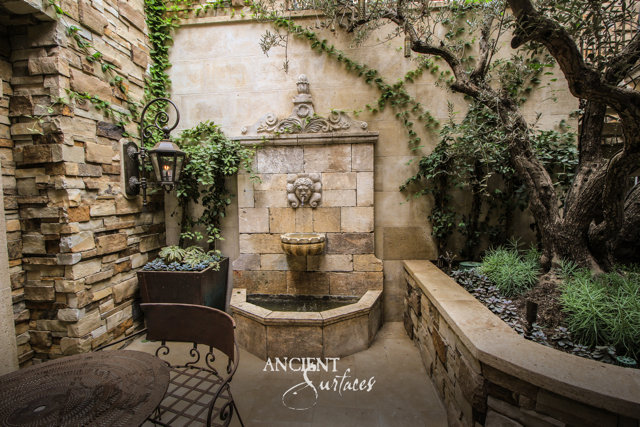 Antique limestone courtyard fountain with a carved crest and lion mask spilling into a scalloped bowl and faceted basin beneath climbing vines