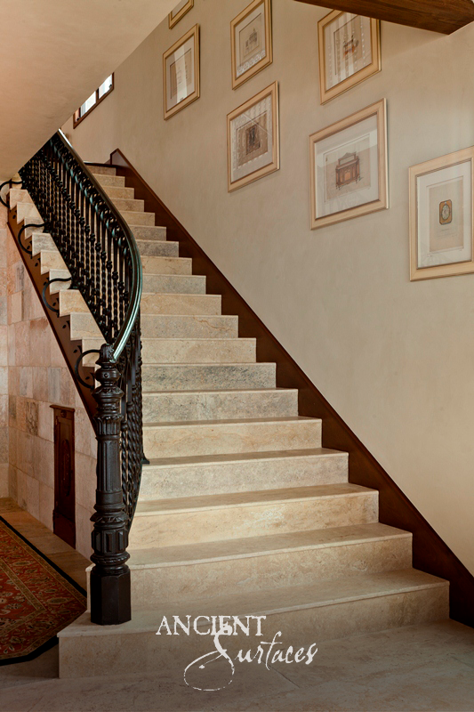 Solid reclaimed limestone stair treads with eased nosings rising beside a black iron balustrade and a limestone clad wall